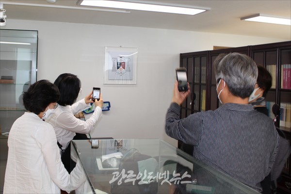 윤공희 대주교 집무 책상 오른쪽 벽면에 걸려있는 팍스 크리스티(PC) 문양을 휴대폰에 담는 PCK회원들 모습.